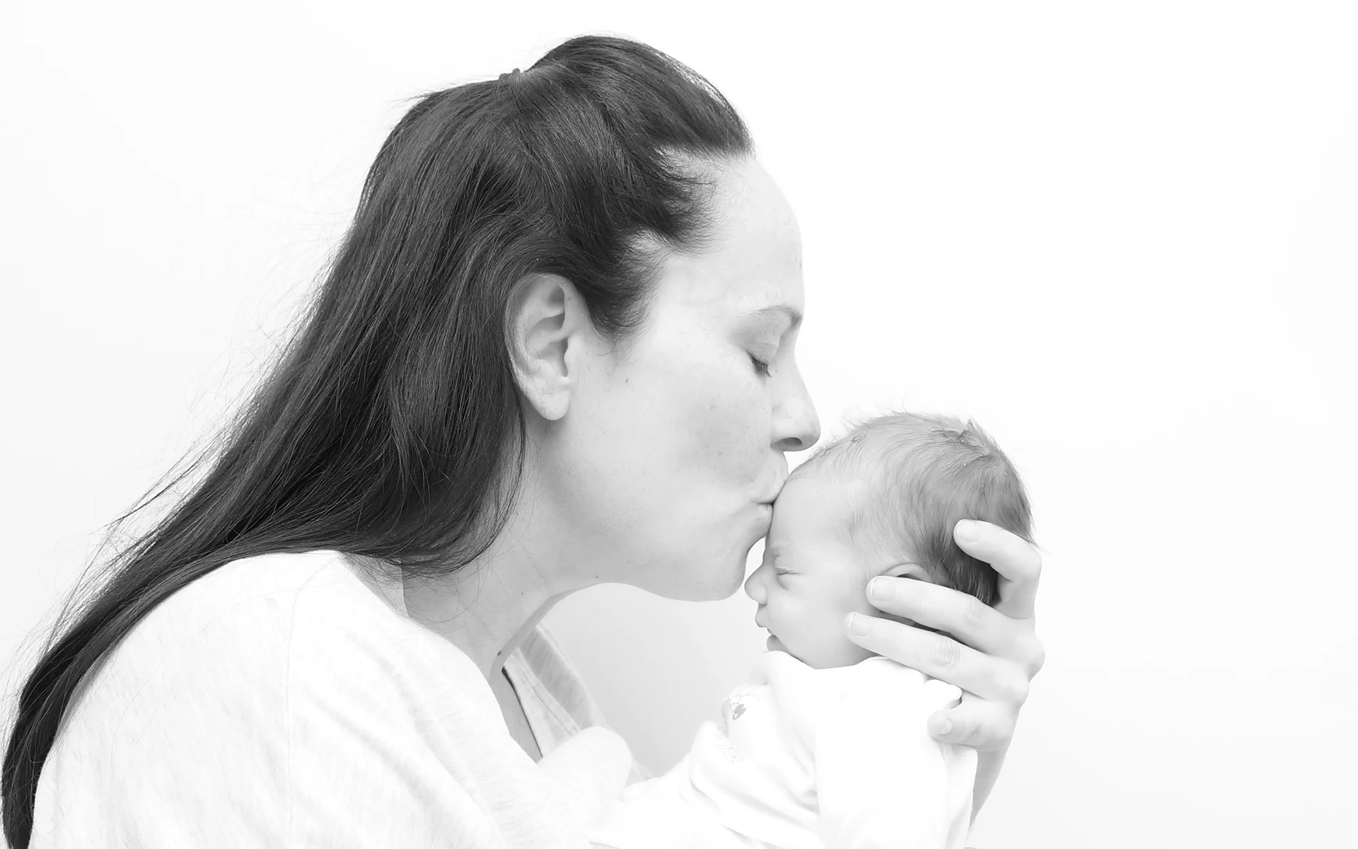 Fotografía de una madre besando a su bebé con luz natural - Etérea Fotografia
